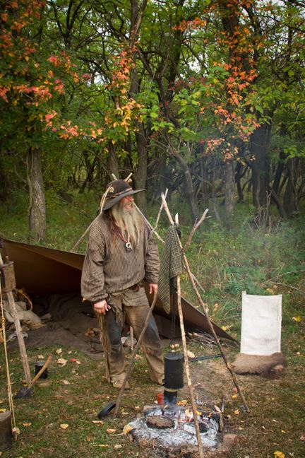 Mountain man standing by a camp fire.